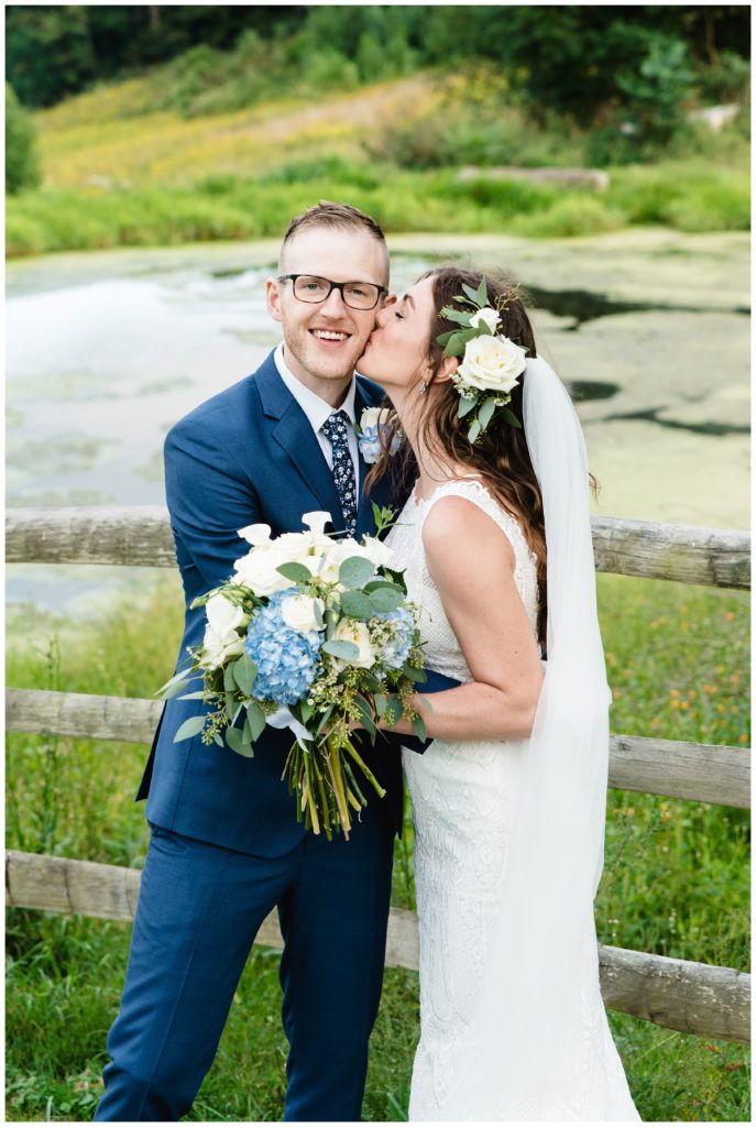 bride kissing groom's cheek in front of pond at the farm house inn