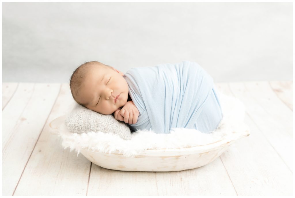 newborn boy wrapped in light blue sleeping in white trench bowl at bridgeville newborn photographer studio