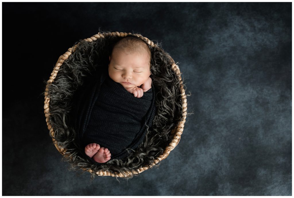 newborn boy wrapped in dark gray in basket on black backdrop at bridgeville newborn photographer studio