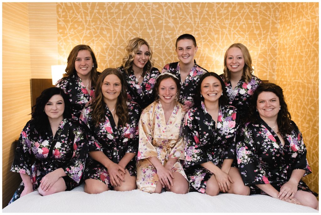 bride sits on hotel bed with bridesmaids in cute floral robes