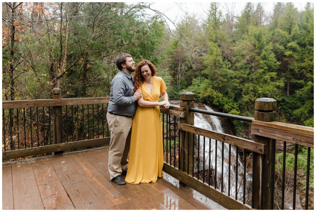 man kisses woman's temple who is in a yellow dress on top of bridge overlooking waterfall at swallow falls