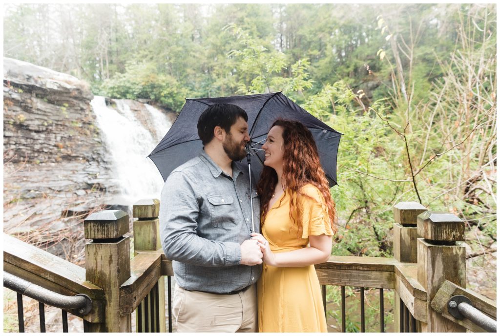 engaged couple looks at each other under umbrella in front of swallow falls waterfall