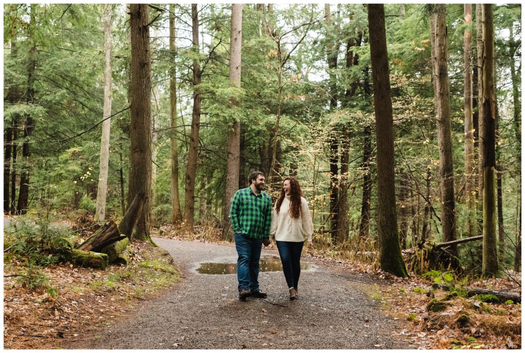 engaged couple holds hands and walks along path at swallow falls during the fall