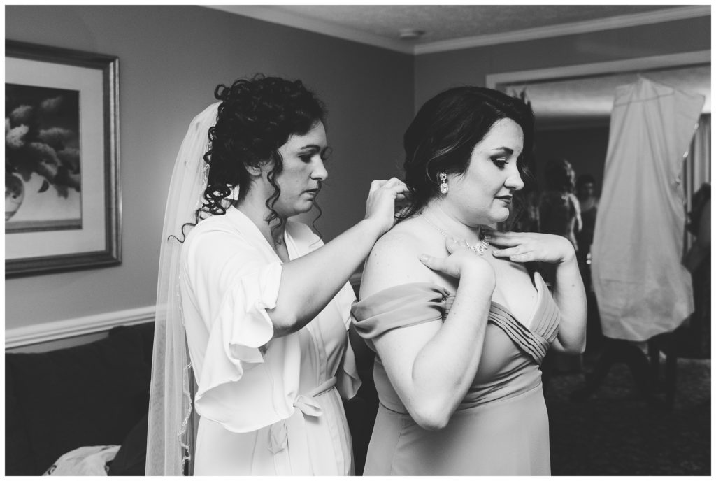 bride helping maid of honor put her necklace on