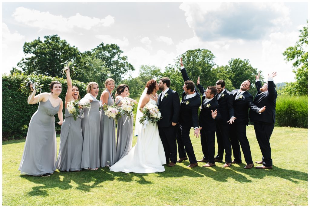 bride and groom kissing on lawn of lakeview golf resort surrounded by bridal party cheering