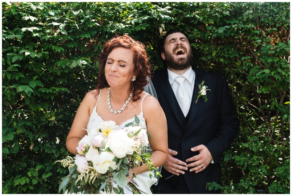 bride and groom laughing hilariously while squishing themselves in a hedge at lakeview golf resort wedding