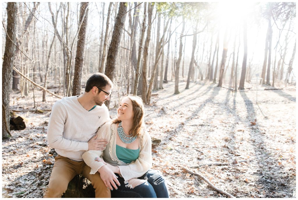 engaged couple sitting on log and looking at each other in woods