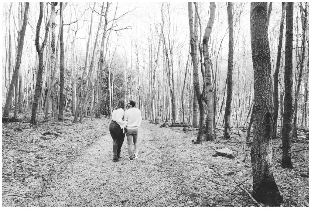 black and white image of engaged couple walking in woods
