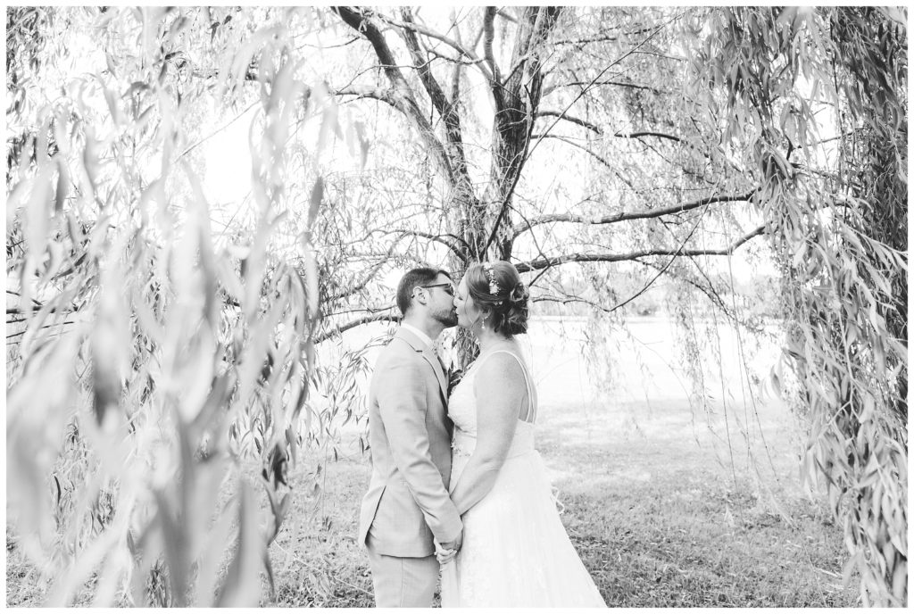 bride and groom kissing under willow tree