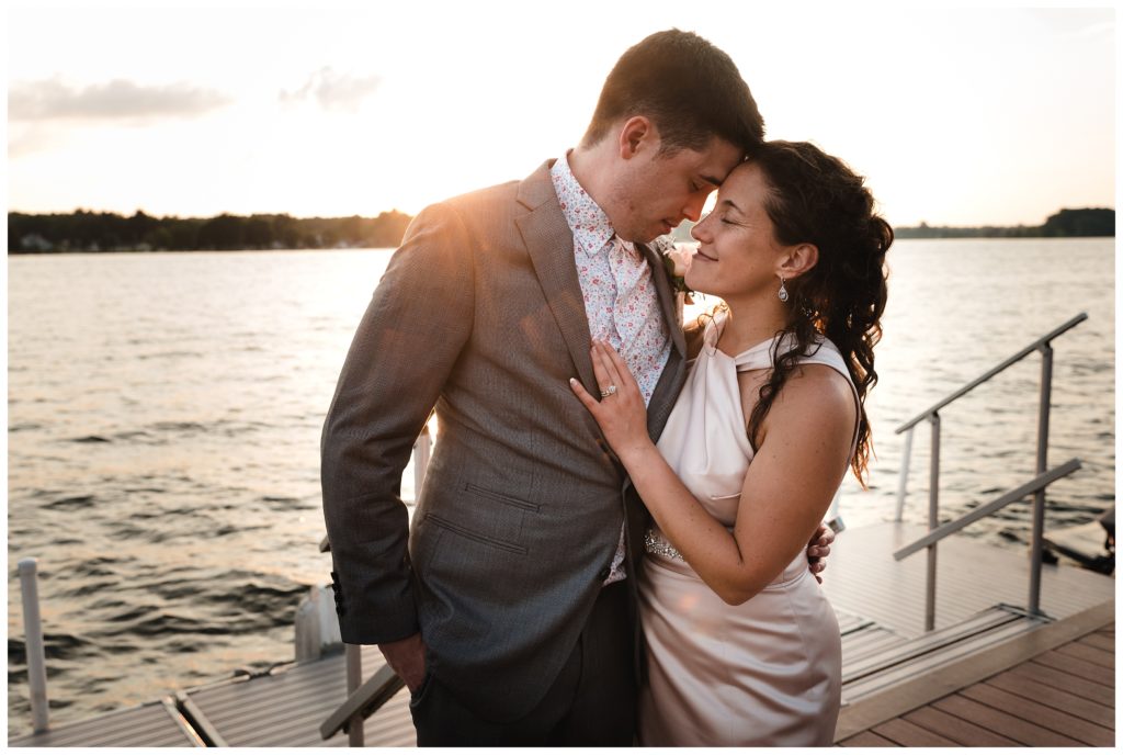 bride and groom leaning foreheads together at sunset on dock