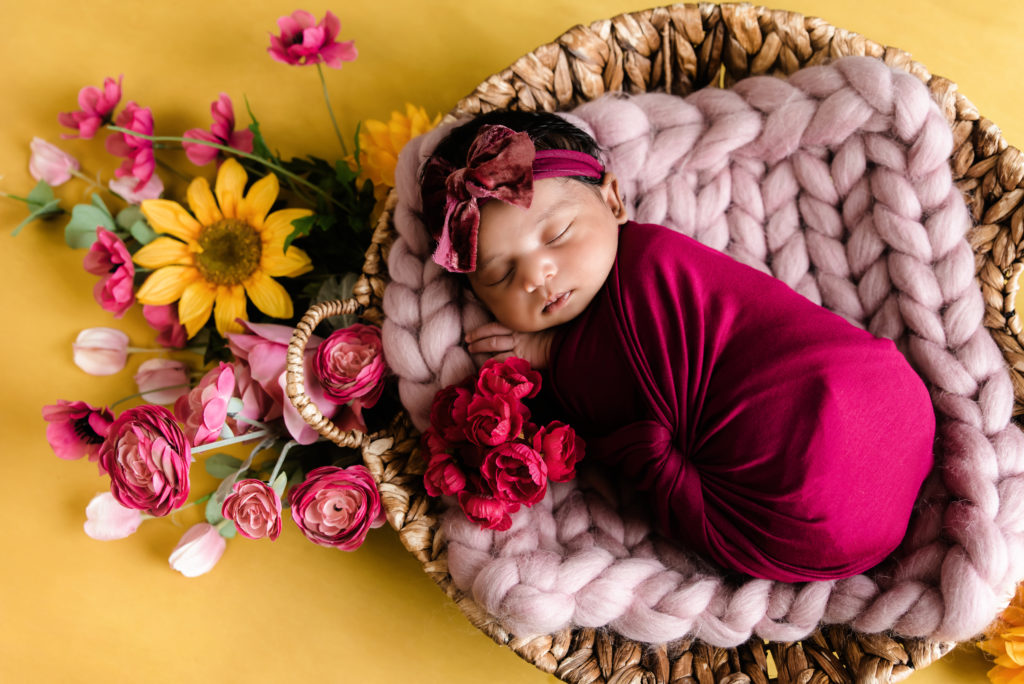 baby girl wrapped in dark pink sleeping in basket by sunflowers | best pittsburgh newborn photographer
