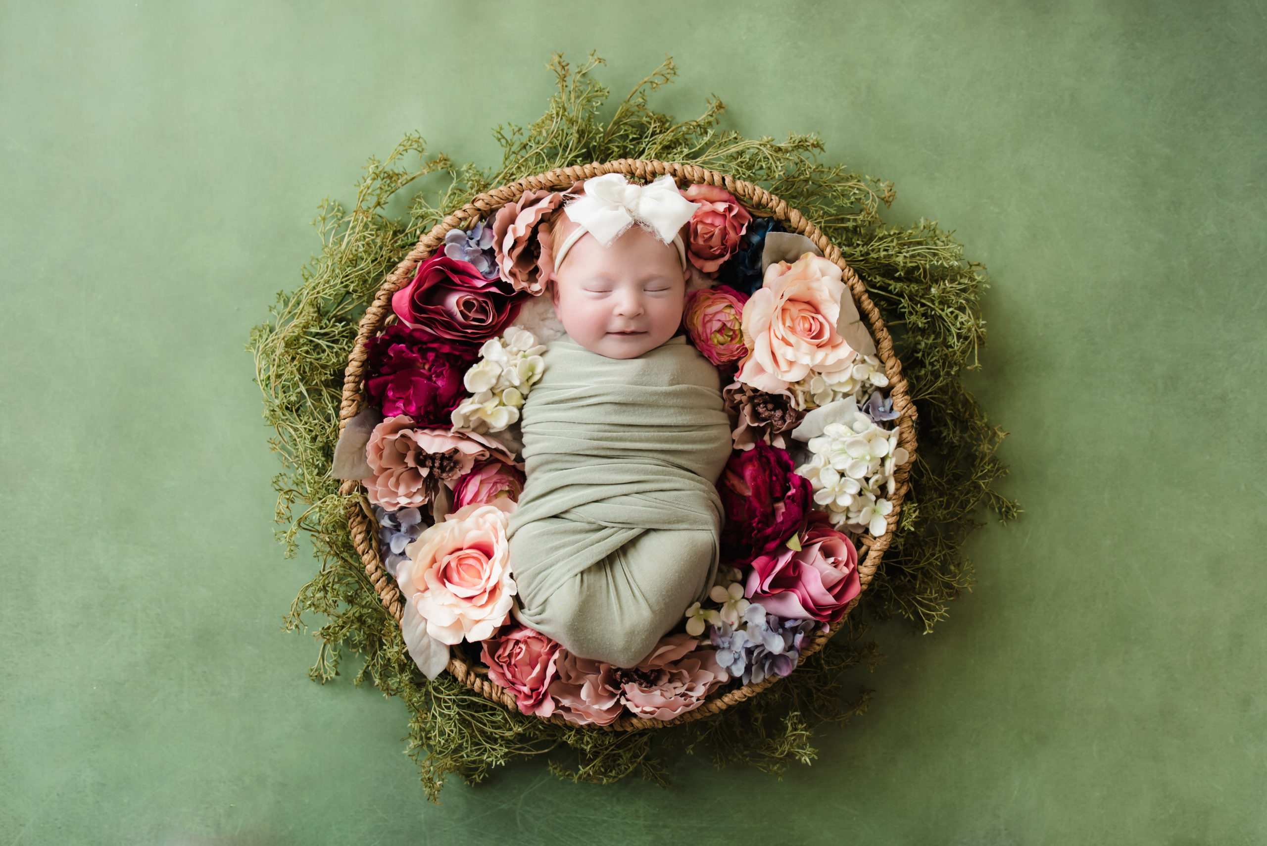 baby girl wrapped in green sleeping in round basket amid pink flowers and smiling | Pittsburgh Baby Photographer - Katie Louise Photography