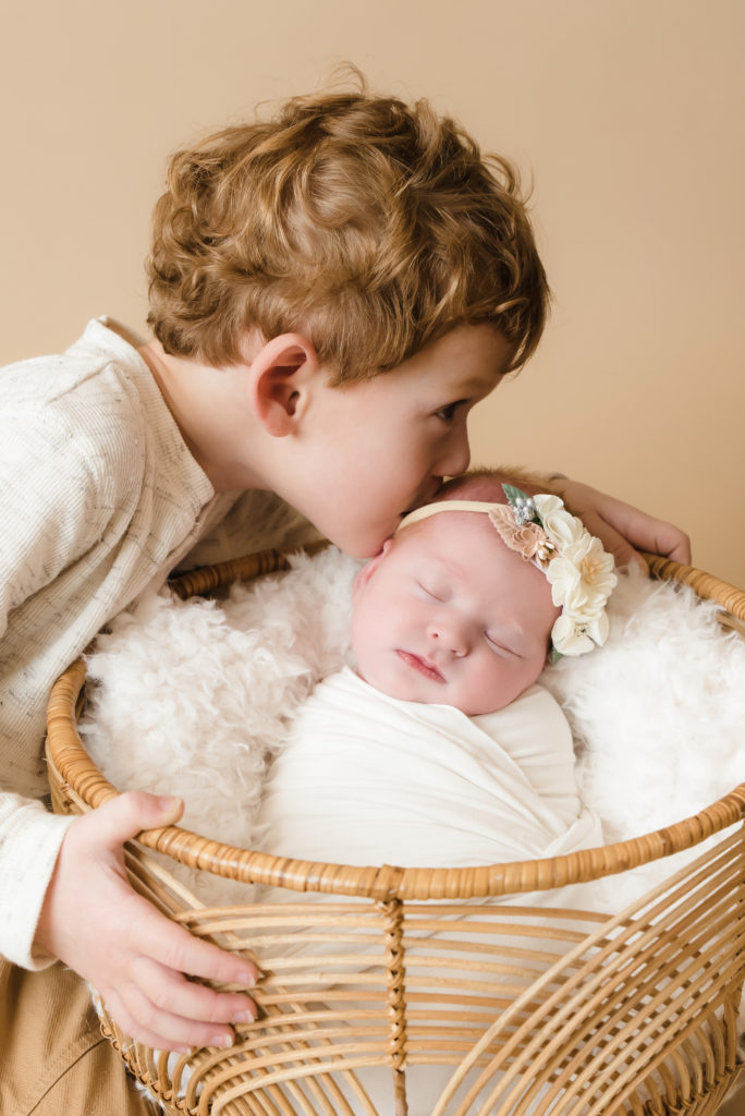 older brother is kissing newborn sister while she's sleeping in a basket