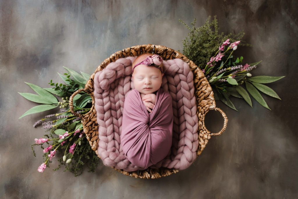 baby girl in purple sleeping in round basket with pink flowers