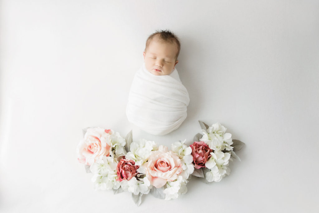 baby girl wrapped in white with pink flowers below her