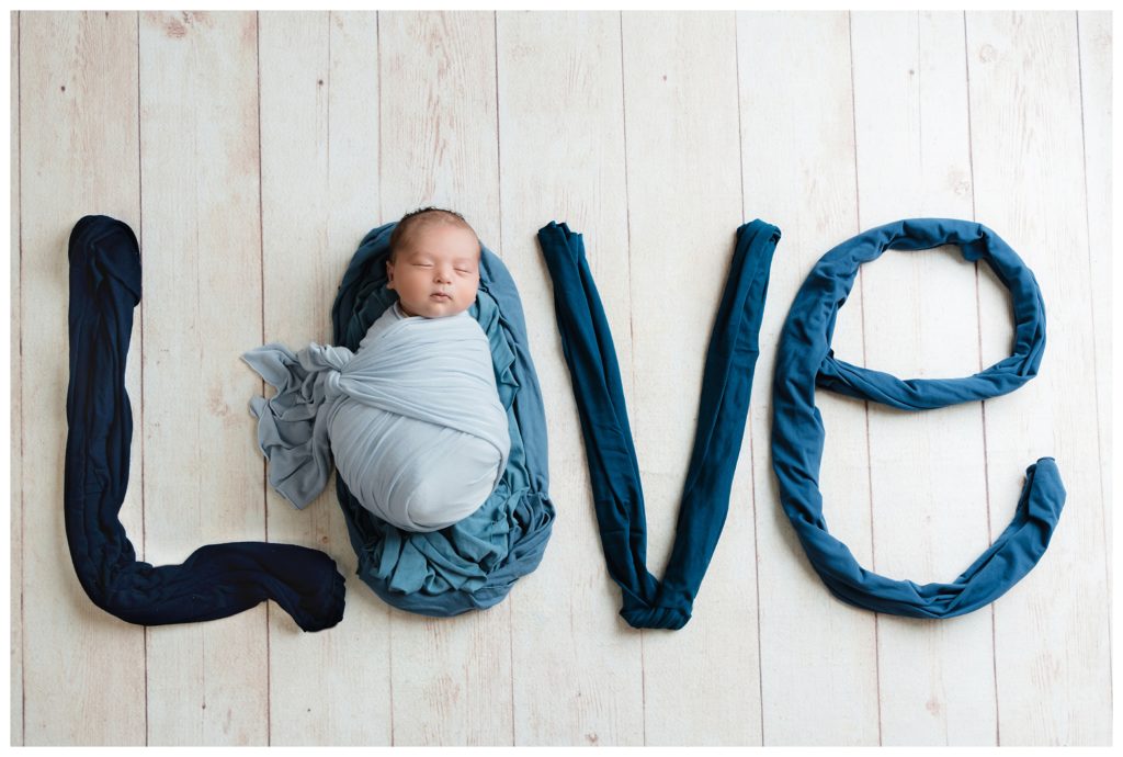 "love" spelled out with different colored blue wraps. Newborn boy is inside the "o."