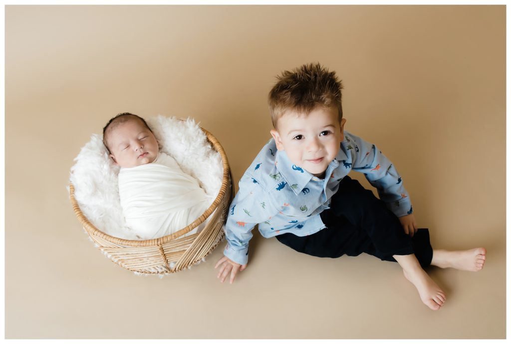 Older brother sits by newborn baby in basket.