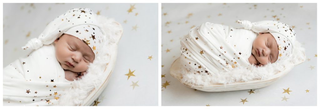 Newborn boy wrapped in white with gold stars sleeps on a white wooden bowl.