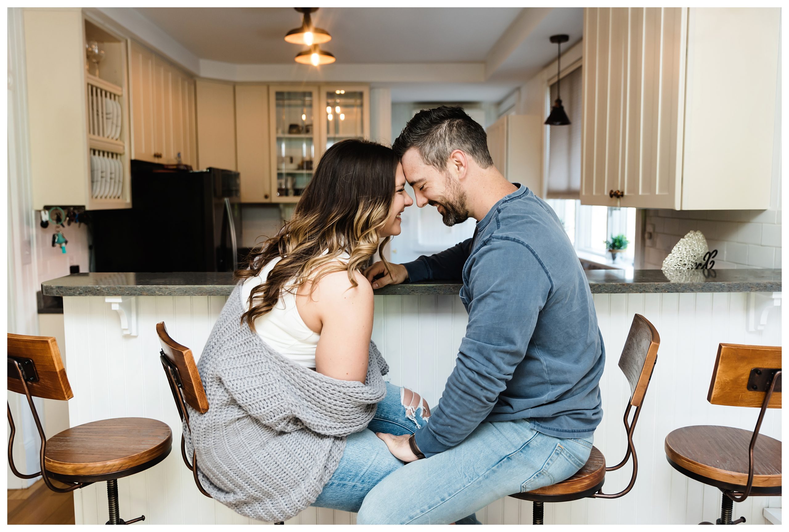 engaged couple sitting on stools in their kitchen with their foreheads touching