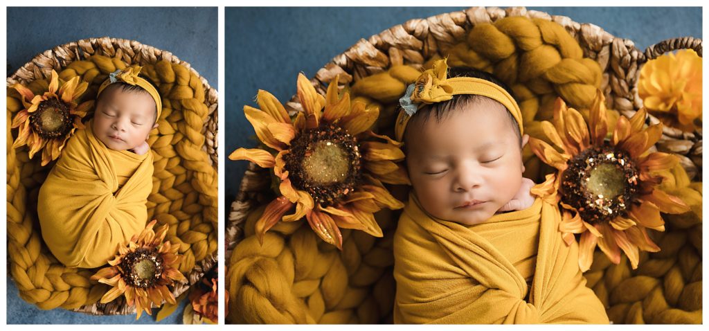 Newborn baby sleeping in yellow wrap on round basket, surrounded by fall blue and yellow flowers.