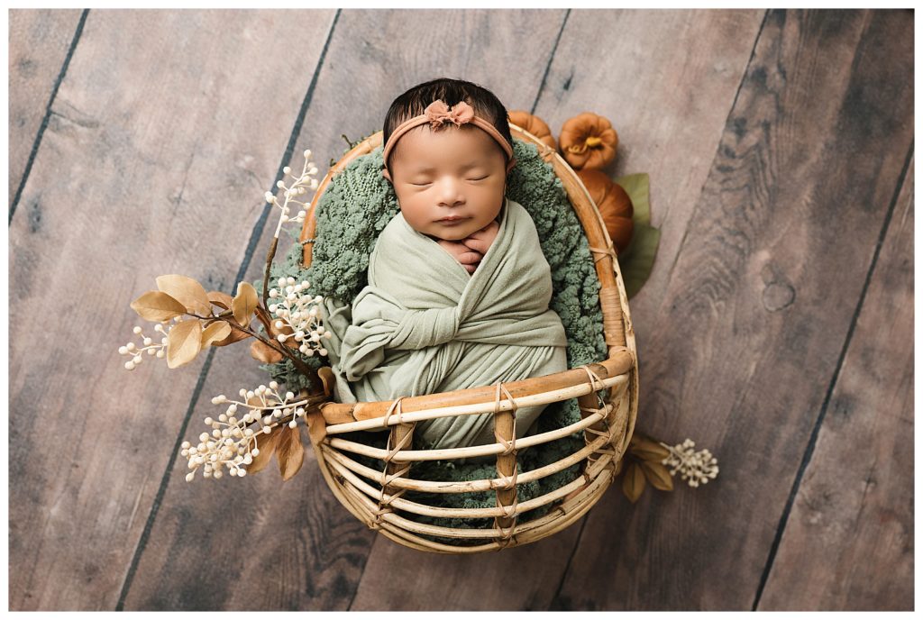 Newborn baby sleeping rattan basket with mini velvet pumpkins beside her during Pittsburgh studio newborn session.
