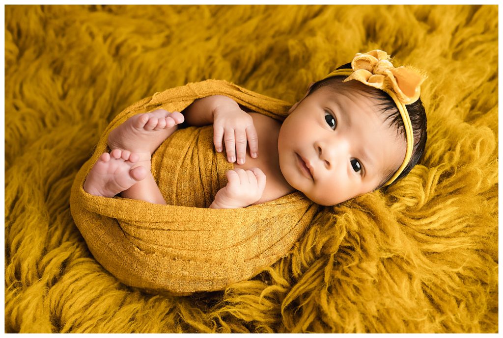 Newborn baby wide awake wrapped in mustard on faux flokati during Pittsburgh studio newborn session.