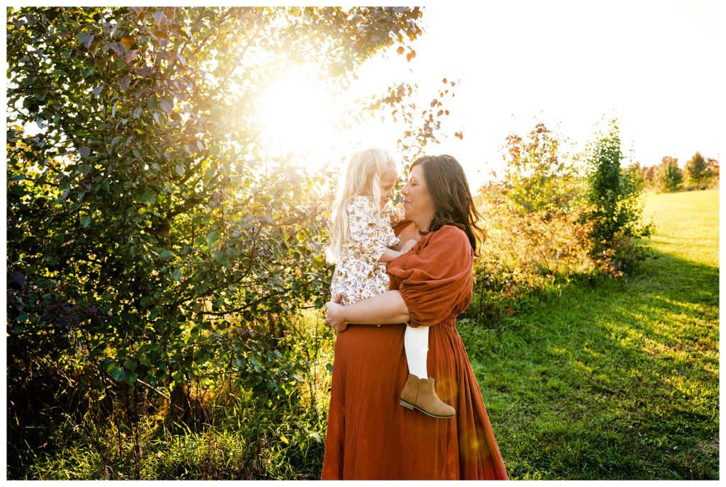 Pregnant mother wears rust maternity dress from reclamation while holding daughter.