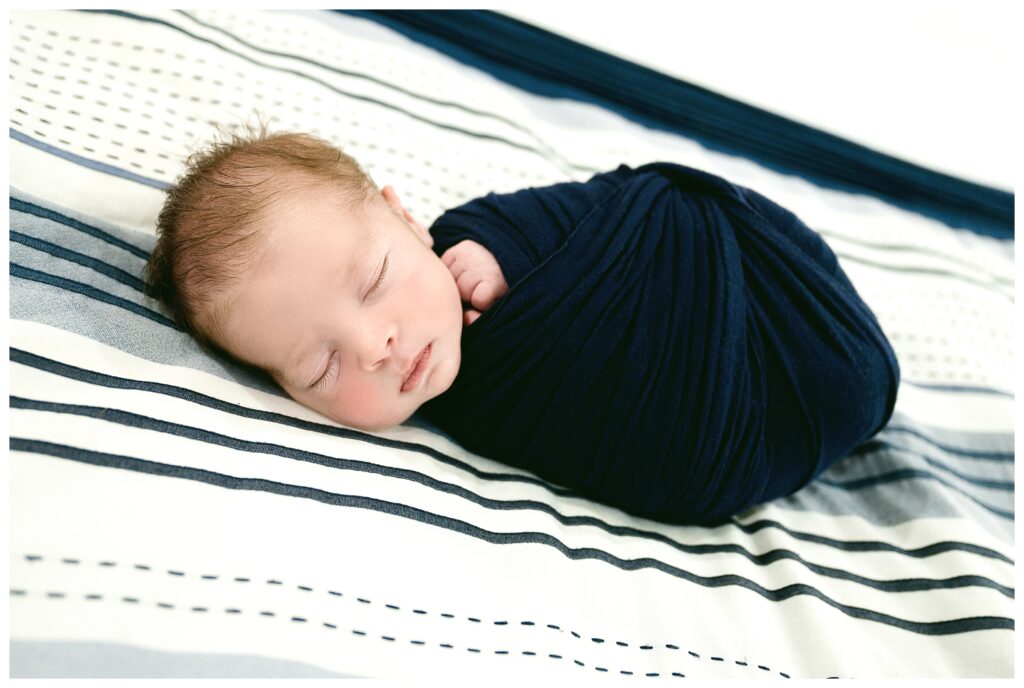 newborn boy swaddled in navy sleeping on mom and dad's bed