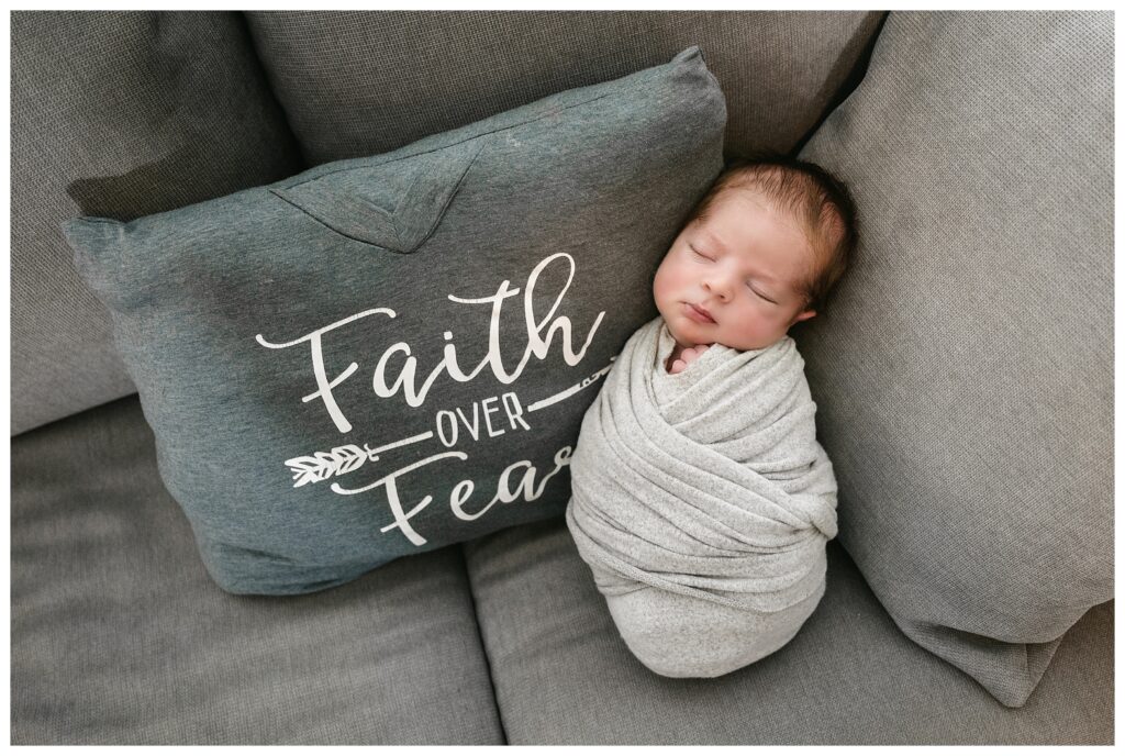 newborn boy sleep swaddled on couch by pillow that read "faith over fear"