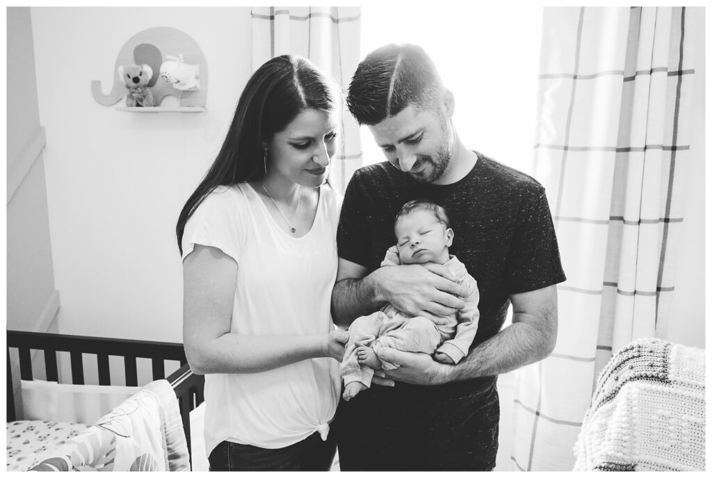 black and white image of mom and dad holding baby and smiling down at him in his nursery