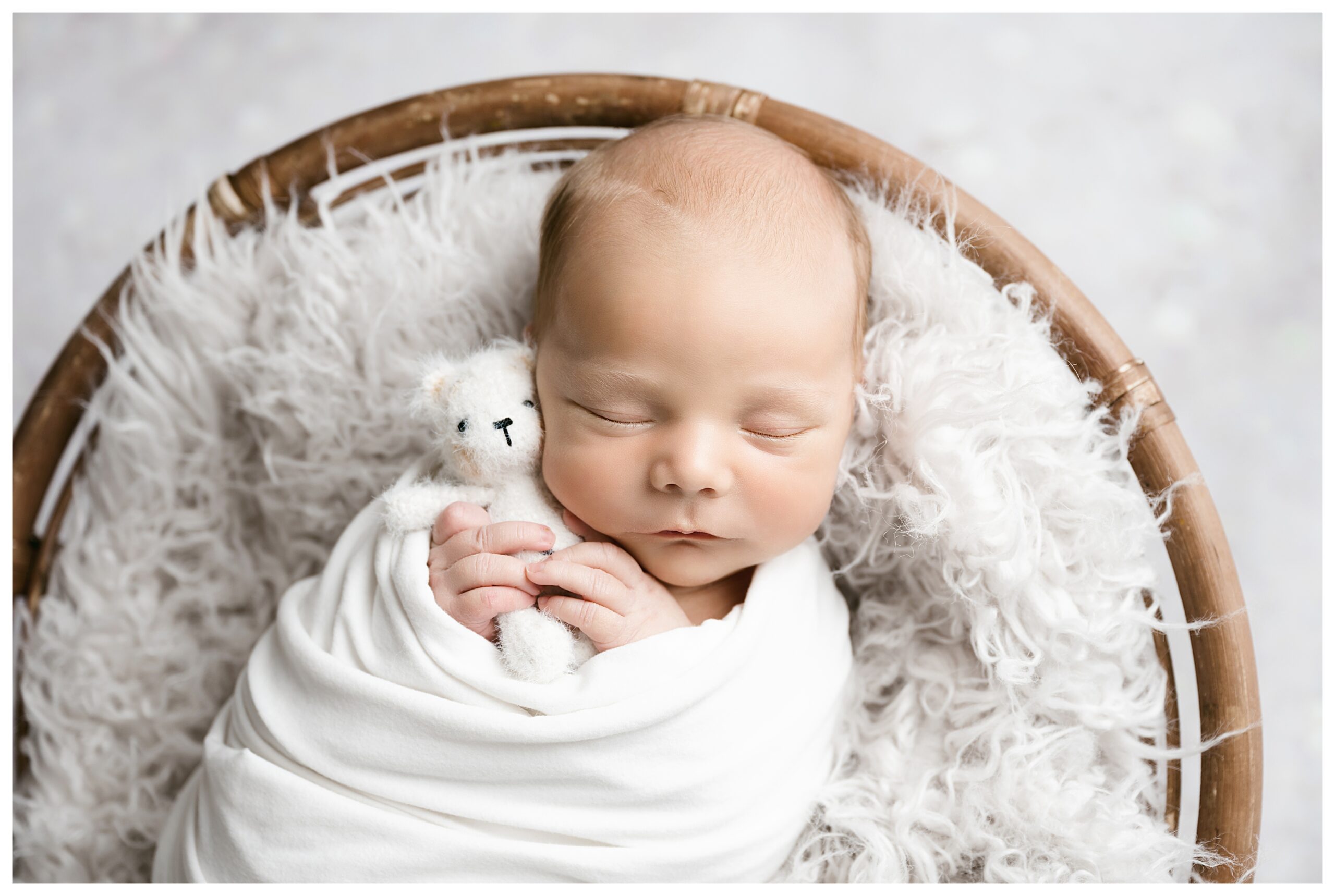 Baby is sleeping and swaddled holding a white teddy bear.