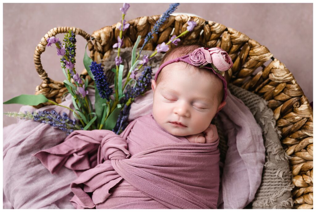 Closeup of newborn girl wrapped in mauve in round basket with lavender.