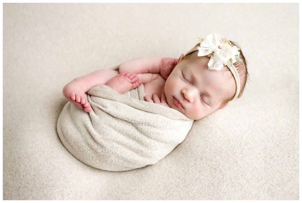 Baby girl sleeps on tan backdrop, wrapped with her toes showing.