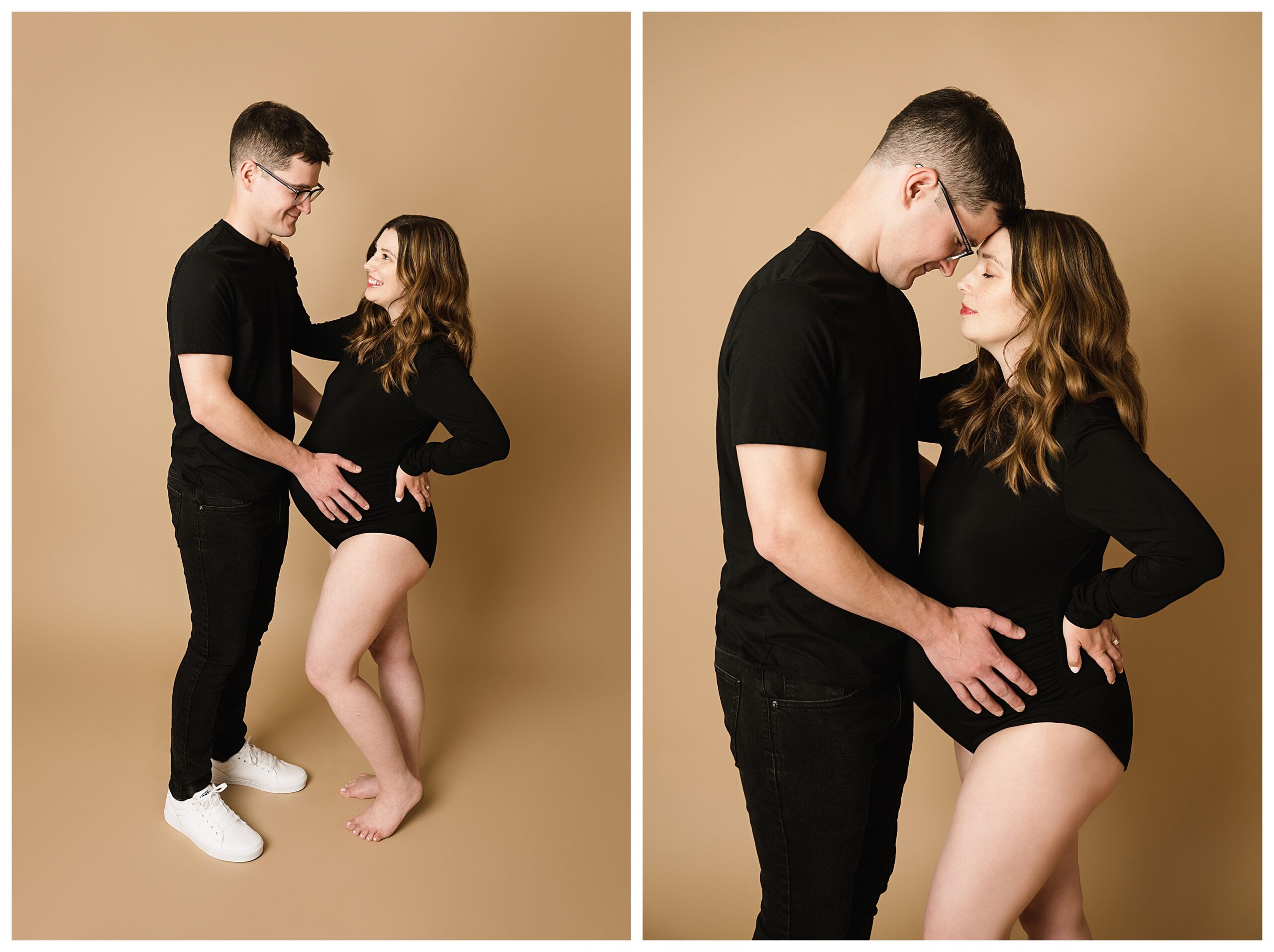 Husband and expecting wife pose looking at each other and then touching foreheads. Husband wears black tee and jeans while pregnant wife wears black bodysuit on tan backdrop during maternity photo session in Pittsburgh.