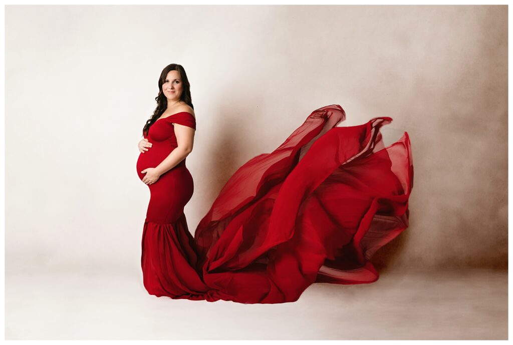 Expecting mom poses in red dress with sweep.