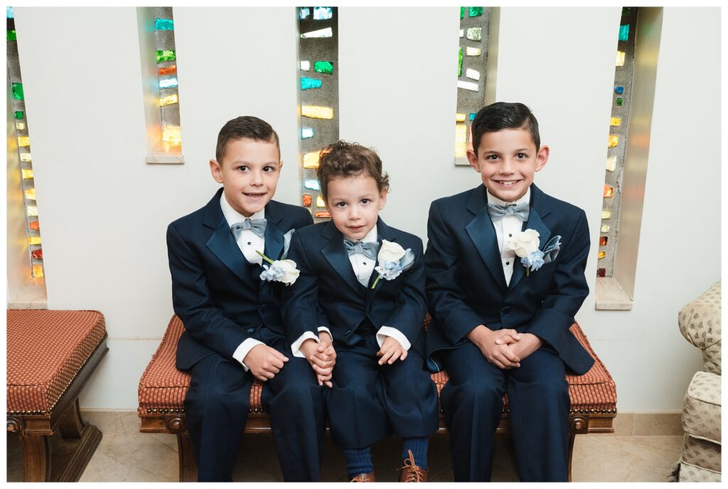 Three little boys in suits sit on bench before ceremony at Holy Cross Greek Orthodox Church