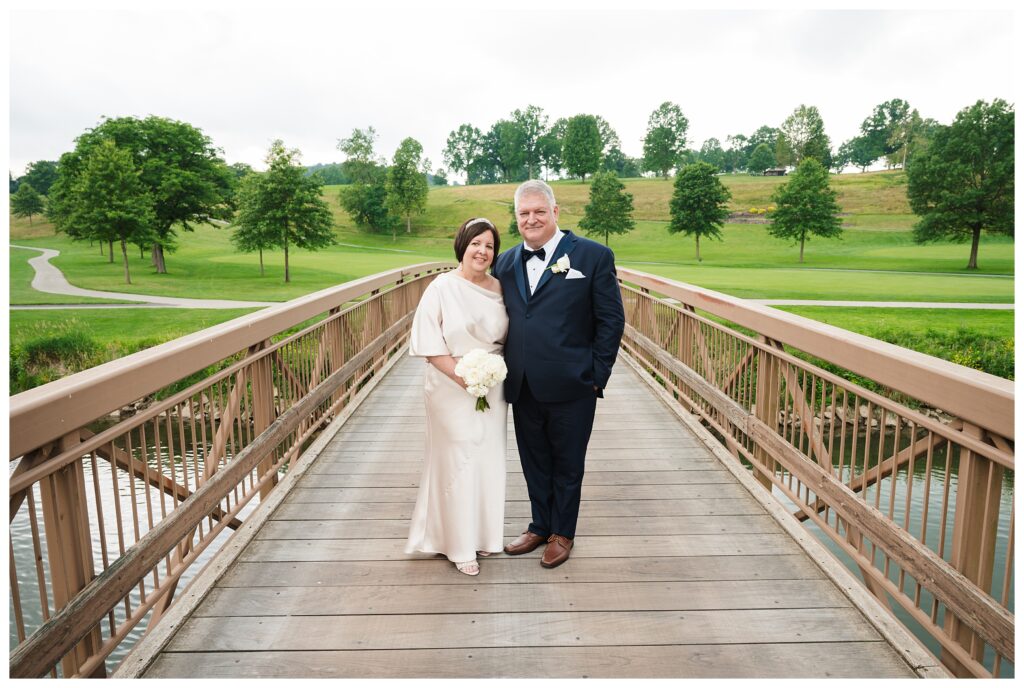 Bride and groom pose on bridge by golf course at valley brook country club.