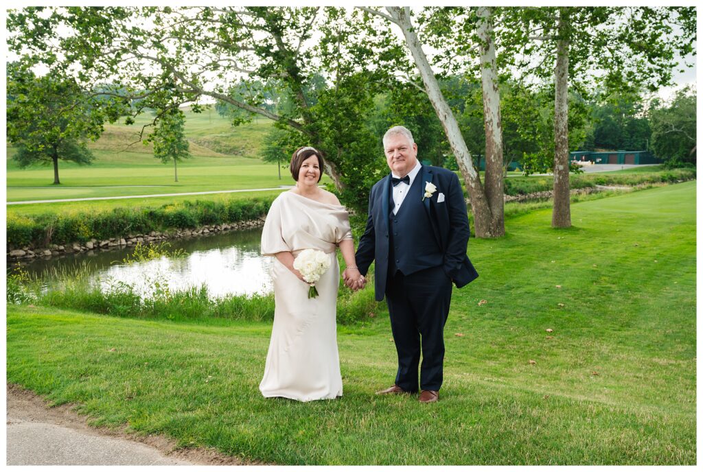 bride and groom hold hands in front of golf course pond at valley brook country club wedding