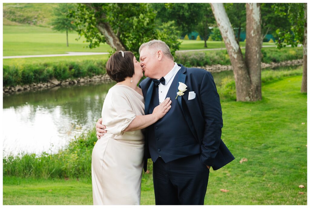 bride and groom kiss in front of golf course pond at valley brook country club wedding