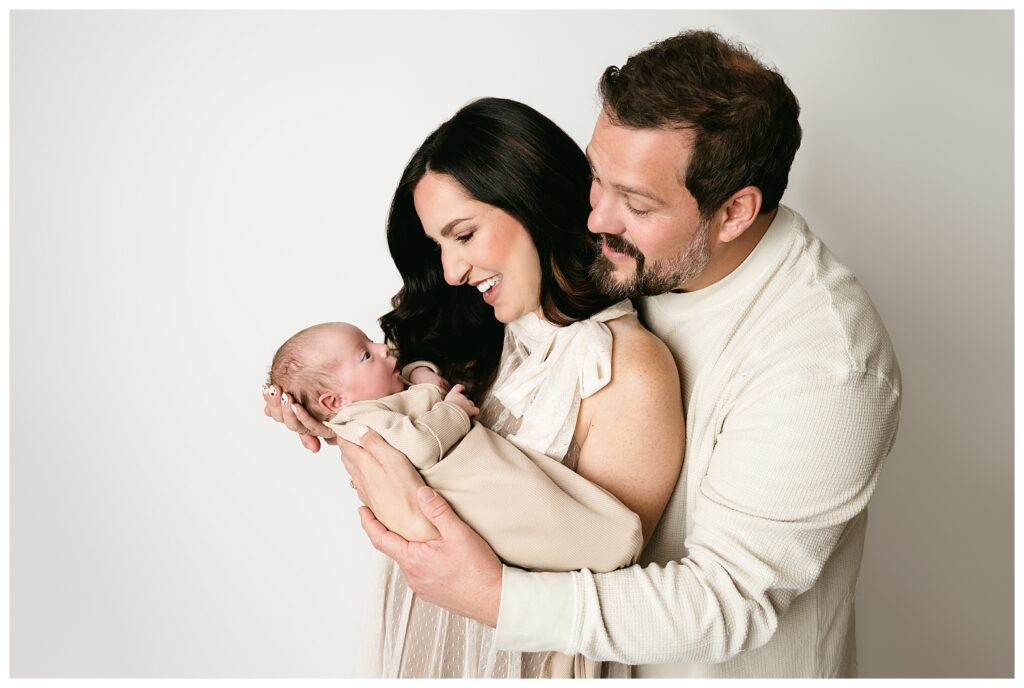 Mom holds newborn boy while dad embraces mom during this neutral studio newborn session.