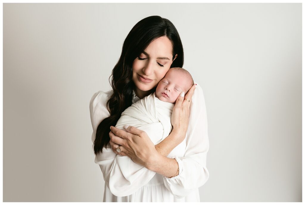Mom closes eyes while snuggling up to newborn son during this neutral studio newborn session.
