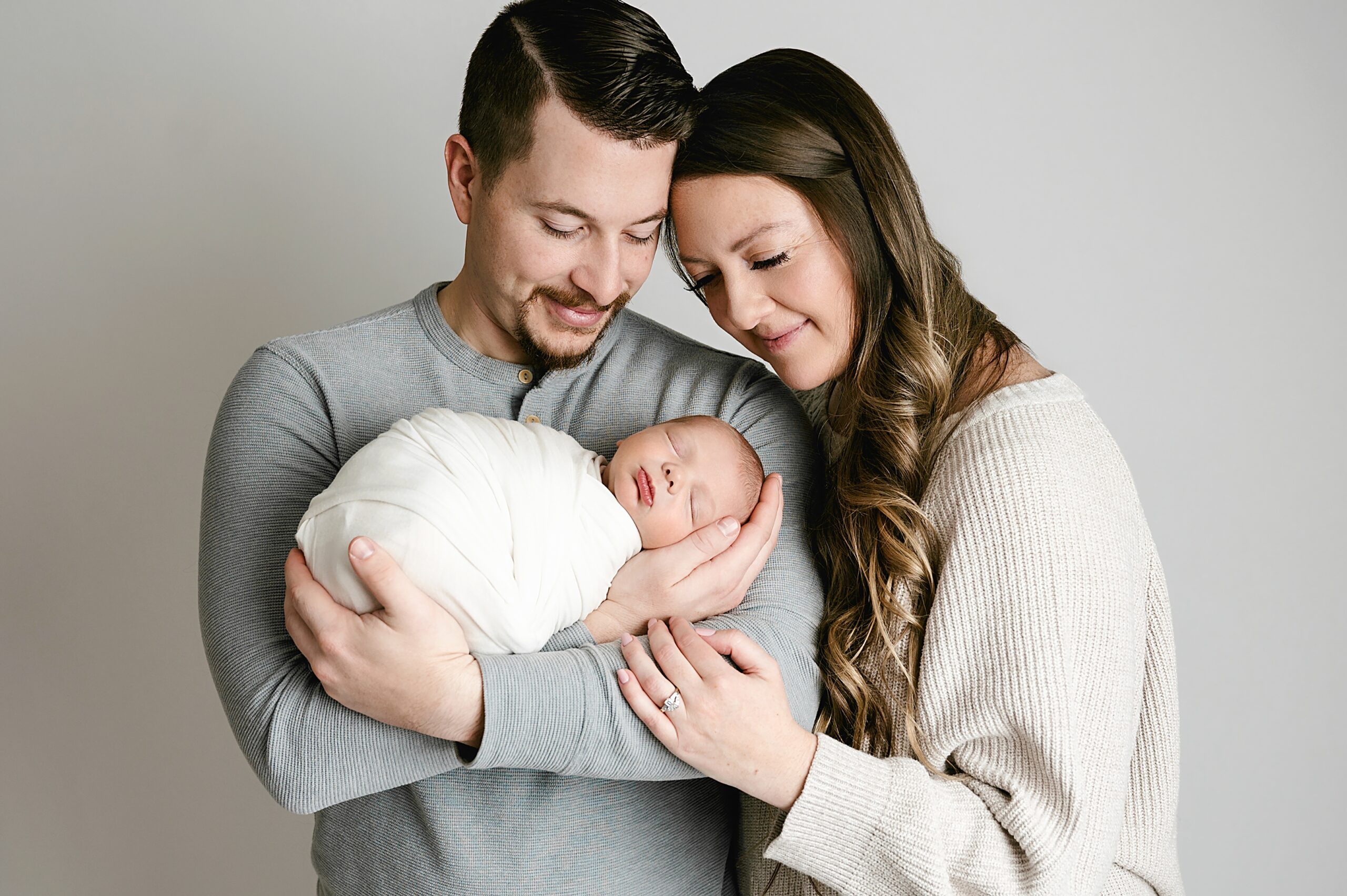 Dad snuggles baby boy to his chest while mom hugs dad's should and they both look down at their newborn during pittsburgh baby photography session.