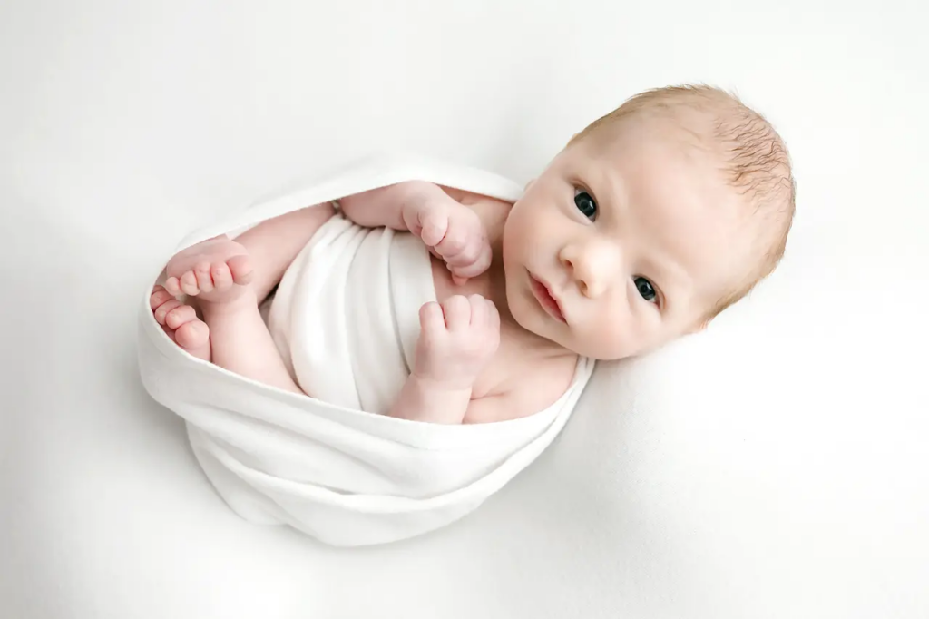 Newborn baby swaddled in white and looking directly at camera during a newborn photography session Katie Louise Photography studio in Bridgeville.